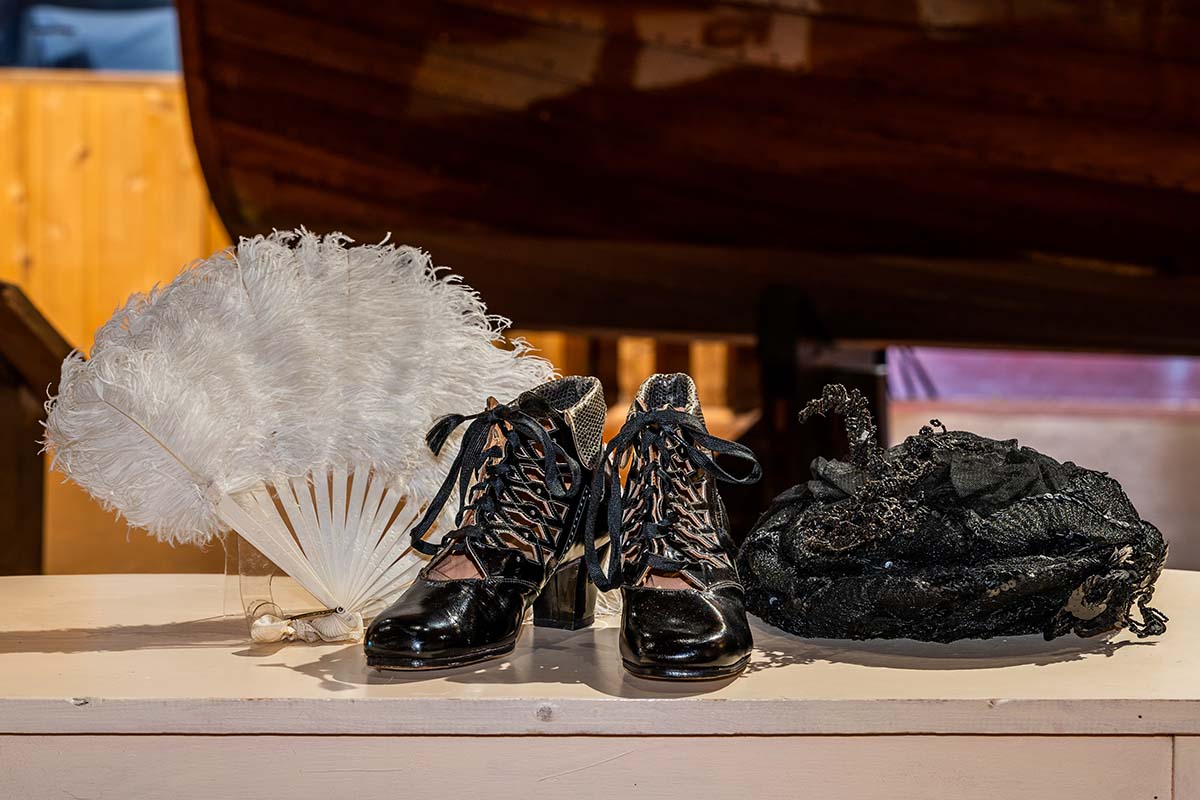An antique white feather fan, black lace-up boots and black hat with sequins 